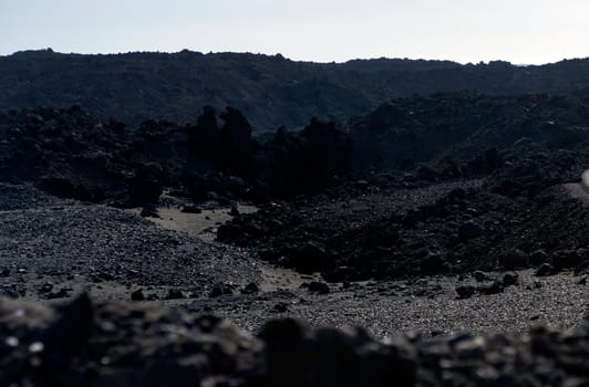 Harsh dramatic volcanic dark soil, lifeless desert with black lava formations and basalt rocks at the foot of the volcano without people.