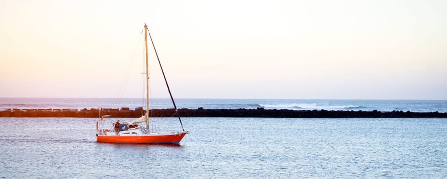 A seascape with a red stylish yacht at sunset sails across the Atlantic Ocean, into the bay during its sea voyage.