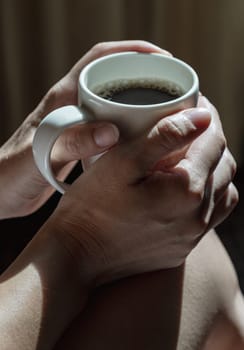 Close-up of Comforting cozy female hands holding a coffee mug with the morning sunlight that shines through. Dark tone, use it as your Wallpaper, Poster and Copy space, Selective focus.
