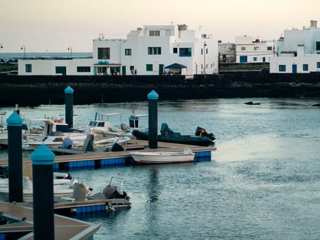 A bay with white boats, yachts on the coast of the Atlantic Ocean with a small beautiful city with white buildings and houses on the Canary Islands, Lanzarote island, Orzola city.