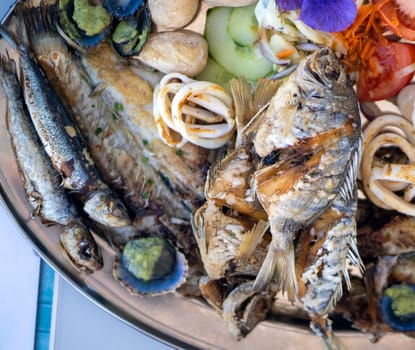 Delicious grilled fish mix plate, a dish with different types of fish, sardines, salmon and seafood, scallops, squid rings from an Atlantic Ocean served in a restaurant in the Canary Islands.