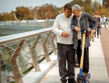 Elderly happy couple have a good and fun time together, on a walk riding a scooter in the park, an elderly man and his wife lead an active and healthy lifestyle.