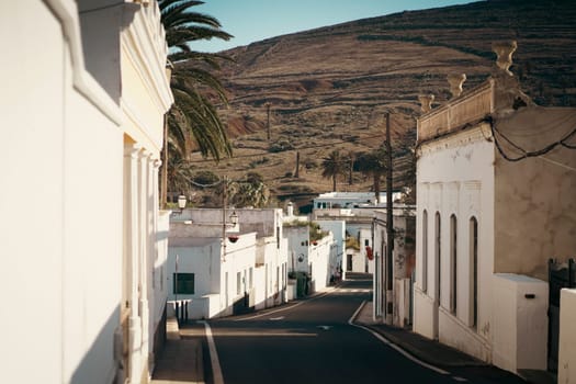 Picturesque streets of a small cozy town with white houses against the backdrop of mountains, view of the road among beautiful buildings on the island of Lanzarote, Canary Islands.