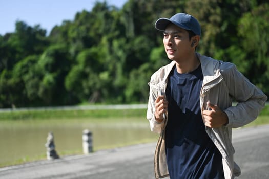Active young asian man jogging by a riverside path on sunny day.