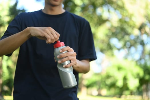 Young sportsman drinking water after exercising in the public park.