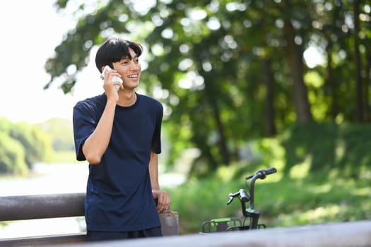 Young adult man having a phone conversation while standing next to a bicycle.