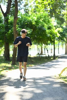 Shot of young man listening to music jogging on a sunny park pathway.