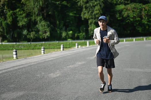 Active young asian man jogging by a riverside path on sunny day.