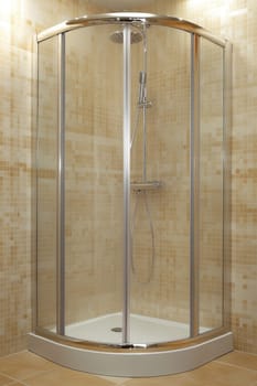 Empty shower cabin with sliding transparent glass doors, chrome shower head and beige tiled walls, creating a clean and modern bathroom space