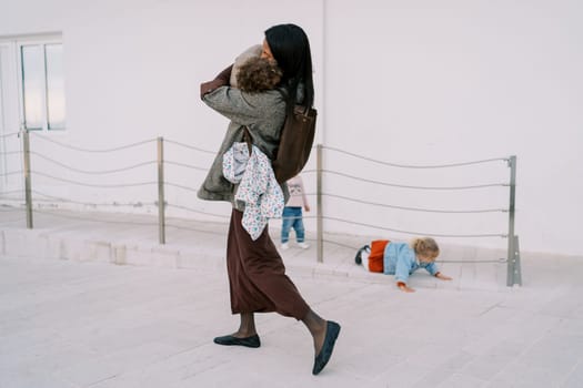 Mom carries a little girl in her arms past her friends playing on the ramp. High quality photo