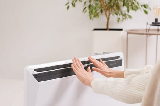 Unwell woman renter in blanket sit in cold living room hand on old radiator.suffer from lack of heat . Unhealthy young woman struggle from chill freeze at home. No heating concept.