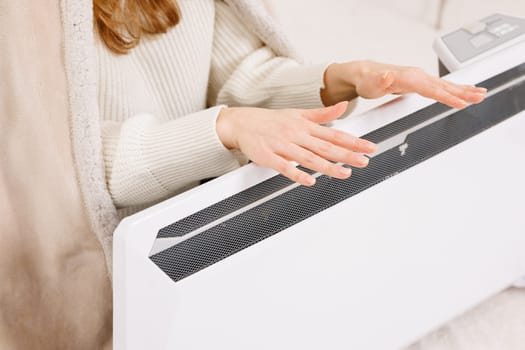 Young woman warming near radiator at home, closeup.