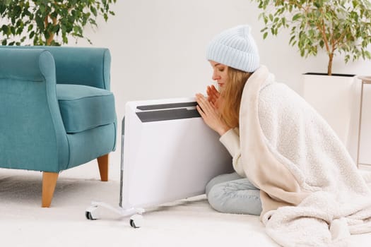 Frozen young woman with plaid warming near radiator at home.
