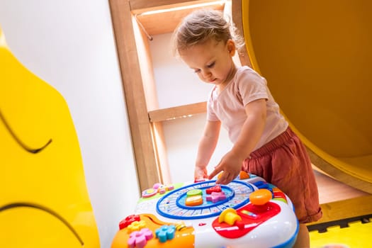 Toddler playing with colorful interactive activity table in a vibrant indoor playroom