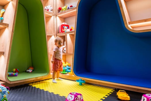 Child exploring a colorful playroom with wooden shelves filled with toys and cushioned seating areas