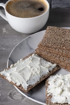 Enjoying crispbread topped with creamy cheese beside a steaming cup of coffee in a cozy setting.