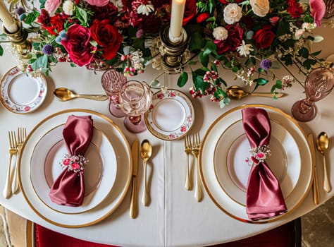 Festive table setting with candles and arrangement of beautiful red flowers. Holiday concept. High quality photo