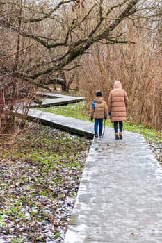 Woman walks with her son on the wooden path walk in the winter park