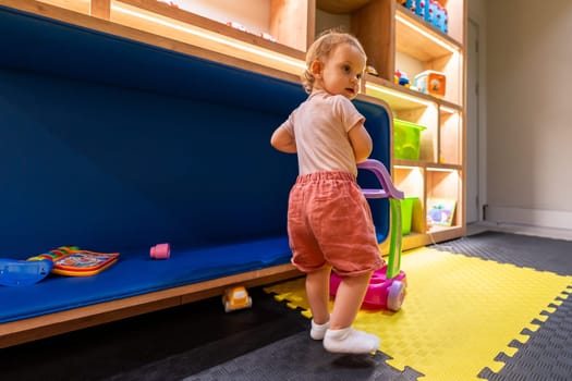 Toddler playing with colorful push toy in modern indoor playroom for kids