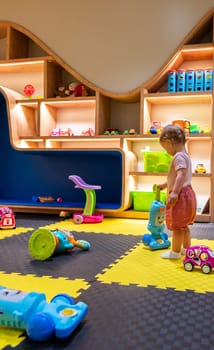 Young child enjoying a playful indoor activity space with toys, shelves, and creative designs