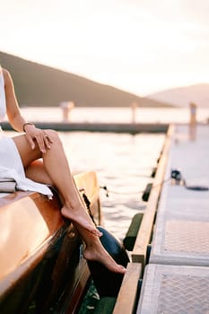 Barefoot woman sits on board a yacht moored at the pier. Cropped. Faceless. High quality photo