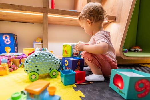 Young child stacking blocks and exploring toys in a colorful indoor playroom