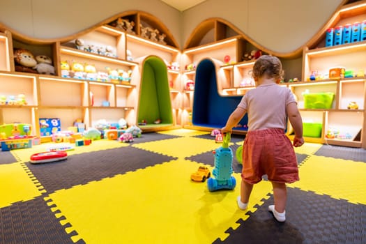 Toddler playing with a colorful vacuum toy in a vibrant playroom with shelves full of toys