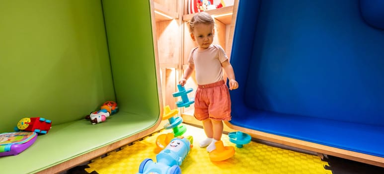 Toddler exploring colorful playroom with educational toys, shelves, and cozy seating areas for creative learning and fun