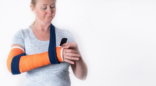 middle aged woman with broken arm in cast hangs her arm in a sling, modern treatment methods, on a neutral background, copy space,