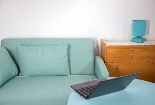 Modern interior with turquoise sofa, laptop on table, wooden cabinet and turquoise lamp on white background, home workspace concept, remote work from home