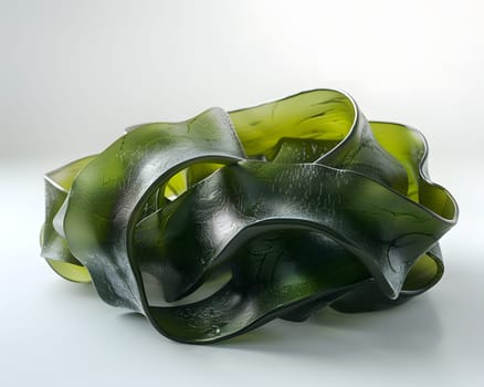 A piece of green seaweed, a plant ingredient, rests on a white surface. It could be used in art, fashion accessories, or as serveware design