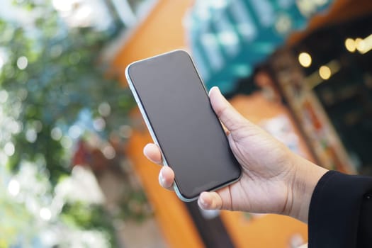 A detailed closeup view of a hand firmly gripping a smartphone while in a lively outdoor area