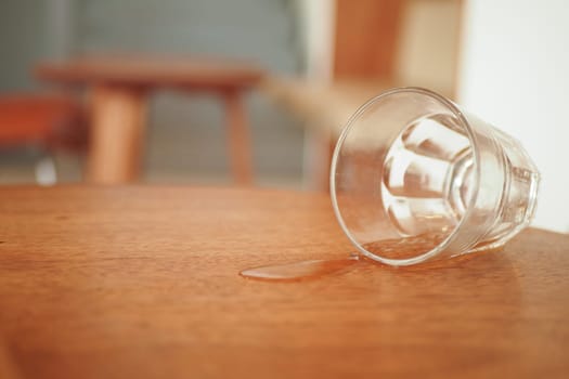 A glass accidentally tipped over on a polished wooden table, causing liquid to spill out