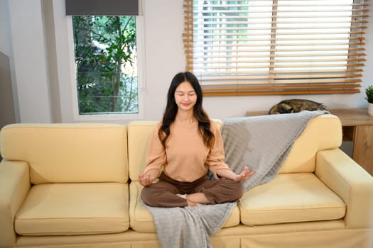Serene young woman practicing meditation on couch in a bright living room.