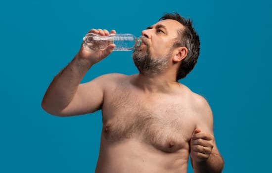 A middle-aged man drinks water from a bottle while taking a break from sports. He appears relaxed and focused on rehydrating after physical exertion, enjoying the moment.