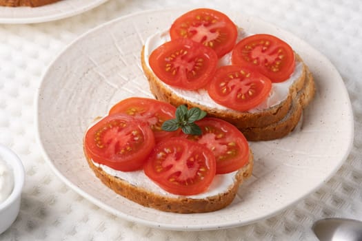 Delicious open-faced sandwiches topped with fresh tomatoes and cream cheese served on a textured white plate.
