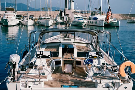 Sailing yacht with two steering wheels and wooden deck is moored at the pier. Back view. High quality photo