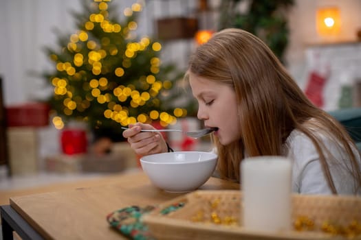 A young girl is joyfully savoring her delicious breakfast in a cozy holiday setting adorned with a Christmas tree