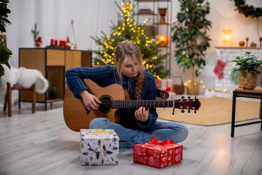 A young person happily playing guitar in a warm setting with Christmas decorations and wrapped gifts