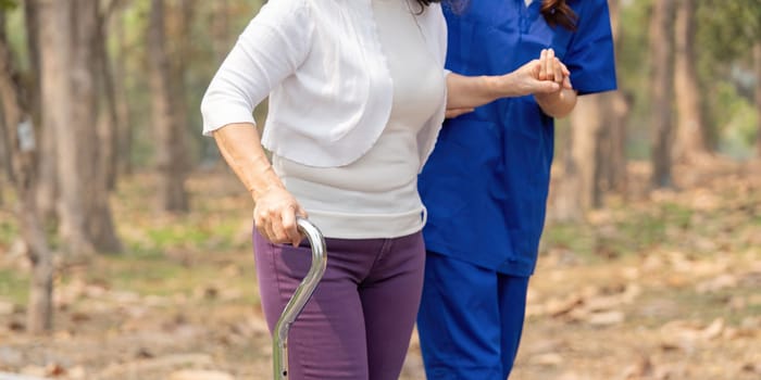 Nurse and senior in elderly care, support or walking with stick at park. Medical caregiver or therapist help patient or person with a disability in retirement or physiotherapy.