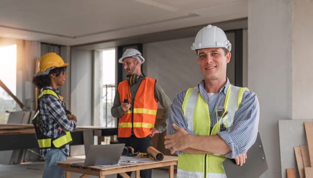 Portrait of an engineer standing and looking at the camera with a team of professional engineers meeting to plan a construction project..