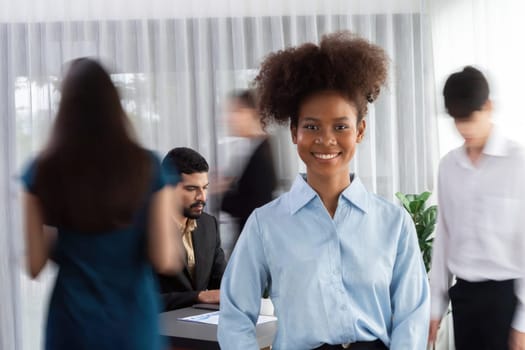 Young African businesswoman portrait poses confidently with diverse coworkers in busy meeting room in motion blurred background. Multicultural team works together for business success. Concord