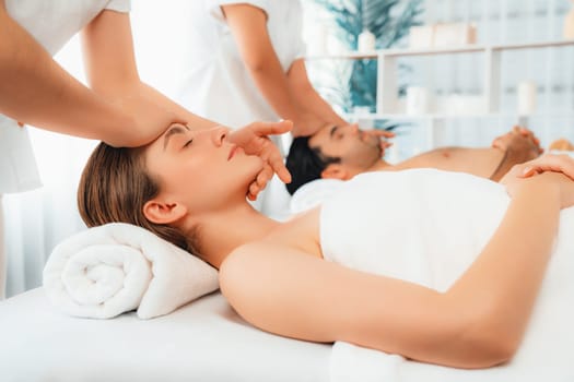 Caucasian couple enjoying relaxing anti-stress head massage and pampering facial beauty skin recreation leisure in dayspa modern light ambient at luxury resort or hotel spa salon. Quiescent