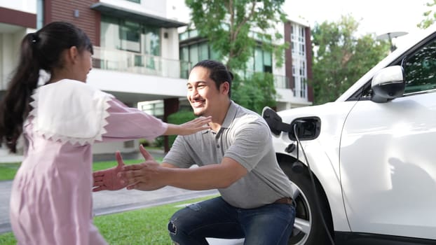 Progressive father and daughter installing plug from home charging station for electric vehicle. Future eco-friendly car with EV cars powered by renewable source of clean energy.