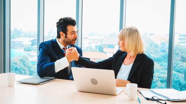 Two happy business people celebrate at office meeting room. Successful businessman congratulate project success with colleague at modern workplace while having conversation on financial report. Jivy