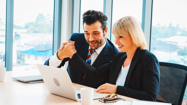 Two happy business people celebrate at office meeting room. Successful businessman congratulate project success with colleague at modern workplace while having conversation on financial report. Jivy