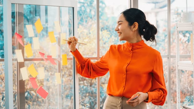 Business people work on project planning board in office and having conversation with coworker friend to analyze project development . They use sticky notes posted on glass to make it organized. Jivy