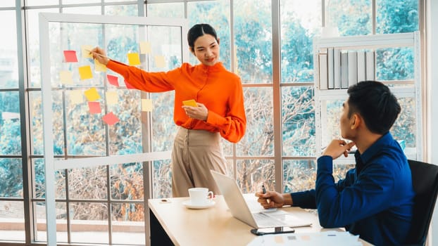 Business people work on project planning board in office and having conversation with coworker friend to analyze project development . They use sticky notes posted on glass to make it organized. Jivy