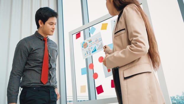 Business people work on project planning board in office and having conversation with coworker friend to analyze project development . They use sticky notes posted on glass to make it organized. Jivy