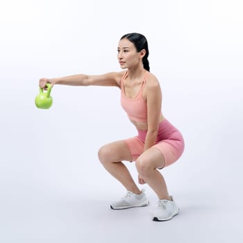 Vigorous energetic woman doing kettlebell weight lifting exercise on isolated background. Young athletic asian woman strength and endurance training session as body workout routine.